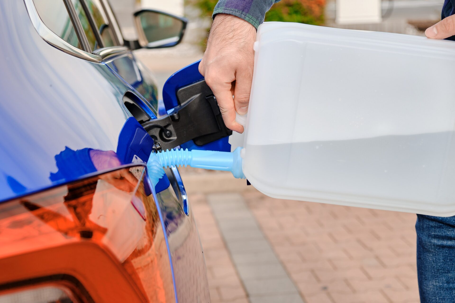 Close up man filling a diesel engine fluid from canister into the tank of blue car